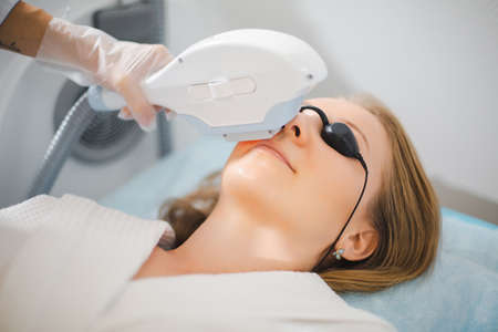 Close up of a young woman face while cosmetologist does the procedure for laser hair removal of...
