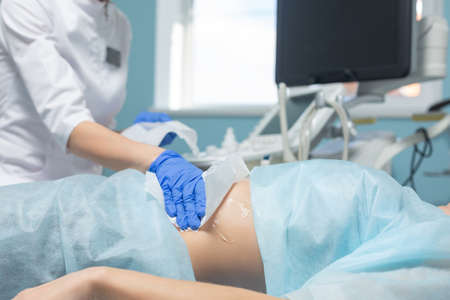 Photo of a doctor wiping medical gel from a pregnant womans abdomen with a napkin after ultrasound diagnosis of the fetus during a scheduled appointmentの写真素材