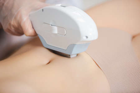 The procedure of laser hair removal of a young girl abdomen with modern tools by a professional specialist in the clinicの写真素材