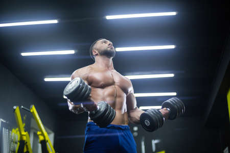 Bottom up view of a strong athlete lifting dumbbells in the gym