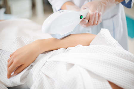 Close up laser hair removal on the arm of a young girl by a professional specialist in a modern...