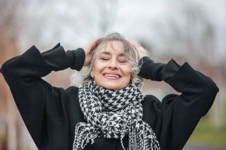 Portrait of a free, independent and happy mature woman in warm clothes against a gray autumn skyの写真素材