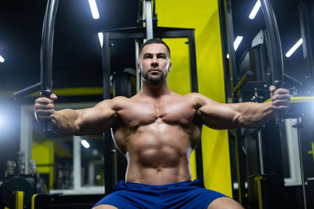 Attractive bodybuilder is working out in a gym training his chest muscles using sports equipmentの写真素材