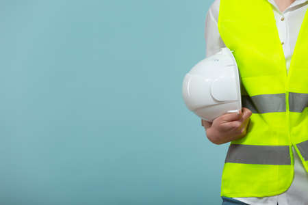 Close-up. Professional engineer. A woman in a bright vest holds a protective helmet in her hands, on a blue background. Copy paste.の写真素材