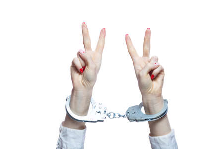 Female hands with handcuffs showing victory sign on white background