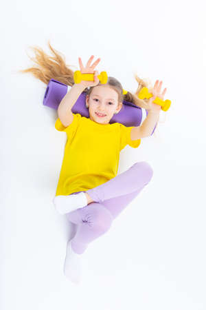 Little cute happy girl lies with dumbbells and gymnastic mat. Isolated on white background. View from above.の写真素材