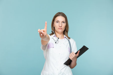 Beautiful woman doctor with a stethoscope and a black tablet, shows a hand sign attention, on a blue background. Copy paste. healthcare concept. Lets stop the disease.の写真素材