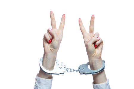 Female hands with handcuffs showing victory sign on white backgroundの写真素材