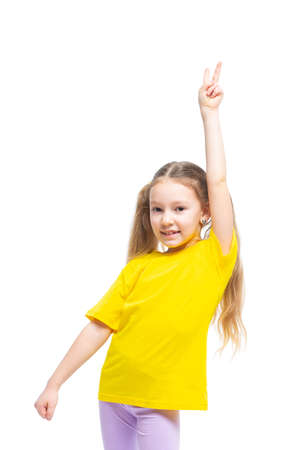 Happy and cheerful child shows victory gesture. The girl is wearing a yellow t-shirt and purple pants.の写真素材