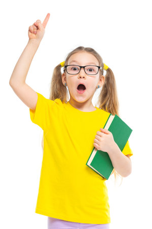 Idea. Points a finger up. Cheerful young child girl with glasses holding a book to study isolated on a white background.の写真素材