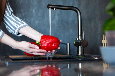 Close-up of a woman in an apron in the kitchen washing vegetables before preparing a vegetarian dish.の写真素材