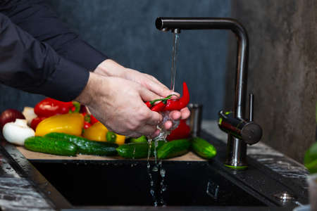 Close-up of a man in the kitchen washing vegetables before preparing a vegetarian dish.の写真素材