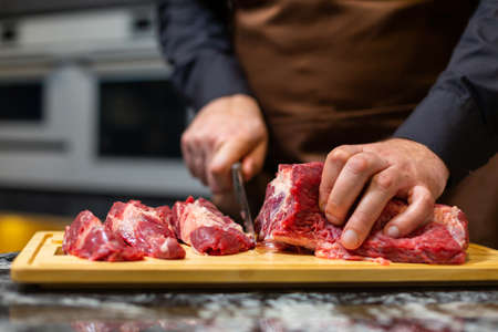 A butcher in an apron in the kitchen cuts pork on a wooden board. Steak.の写真素材