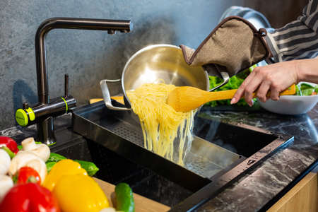 Close-up. A woman in an apron cooks spaghetti in the kitchen.の写真素材