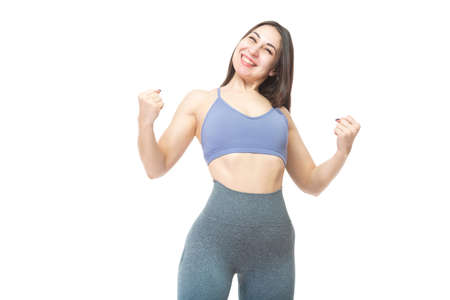 A beautiful, athletic, slim, smiling and cheerful woman shows a gesture with her hands, symbolizing victory, success, class. Lifestyle concept with sports and gym. Isolated on white background.の写真素材