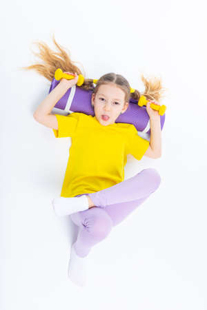 Little cute happy girl lies with dumbbells and gymnastic mat. Isolated on white background. View from above.の写真素材