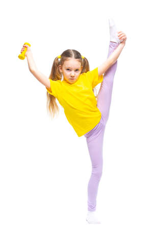 Little cute happy girl with dumbbells performs stretching while standing. Isolated on white background.の写真素材