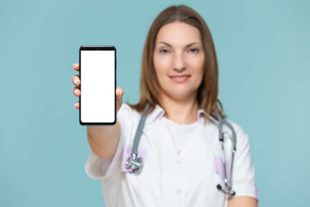 Woman doctor with a smartphone, on a blue background. Place for advertising. Copy paste. healthcare concept.の写真素材