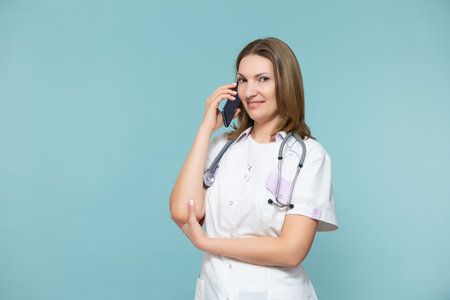 A woman doctor with a smartphone conducts an online consultation, supports the patient by phone, on a blue background. Copy paste. Distance healthcare concept.の写真素材