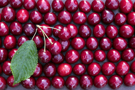 Fresh sweet cherries bowl with leaves on nature background, top view