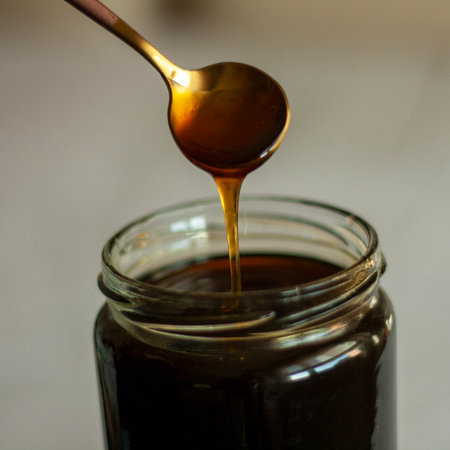 Honey dripping from a spoon into a glass jar, close-upの写真素材