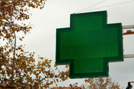 <p>luminous green cross indicating that a pharmacy remains open in the city of Madrid</p>の写真素材