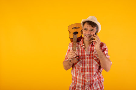 Man dressed in a cheerful and youthful way using his mobile phone and carrying a ukuleleの写真素材