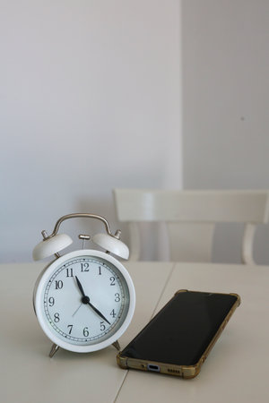An analog clock next to a cell phone on a white background symbolizes the passage of time spent in front of screens.の写真素材