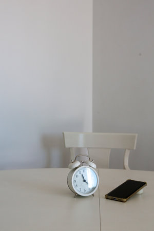 An analog clock next to a cell phone on a white background symbolizes the passage of time spent in...