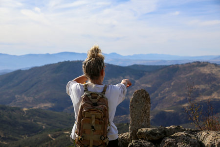 Blonde woman with a bun looking at the mountains after walking along the paths accompanied by her dogの写真素材
