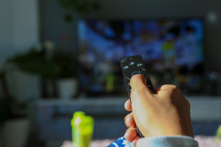 Woman's hand holding a remote control pointing at the television
