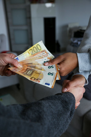 Two women closing a deal, handing over cash and shaking hands; one with light African American skin...