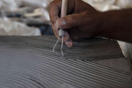 Close up of male sculptor holding tool and making art on clay. Clay master moulding. Clay modelling.