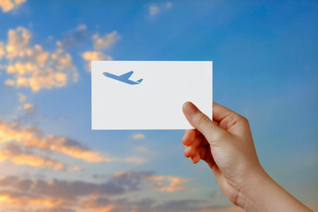 Man's hand holding airplane symbol paper in sky. Concept of journey, travel, dream, freedom. Hand is holding paper airplane against blue sky with empty space for text.の写真素材