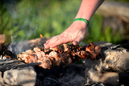 Man cooking marinated shashlik, lamb meat grilling on metal skewer, close upの写真素材