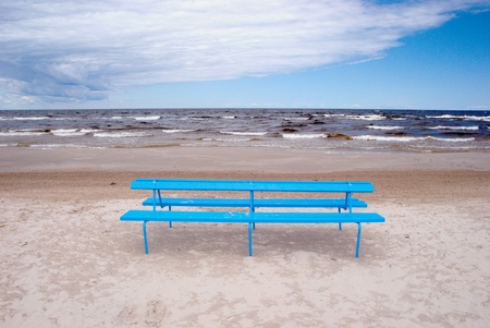 Blue bench on the beach sand near the sea.の写真素材