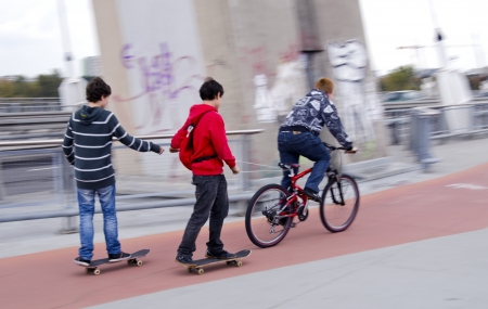 Teenagers riding bikes and skateboards on urban bicycle trail.のeditorial素材