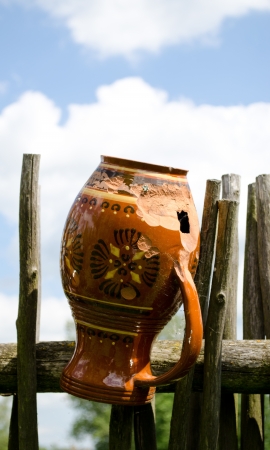 Clay broken pitcher hangs on wooden fence from woven tree branches  の写真素材