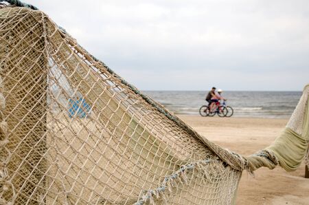 Beach fence decorated with net and cyclists going on sea shore coastline  の写真素材