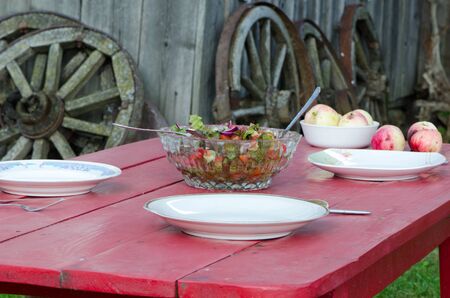 Glass dish full of salad and ecologic apples on wooden table in rural homestead  Wooden cart wheels on background  の写真素材