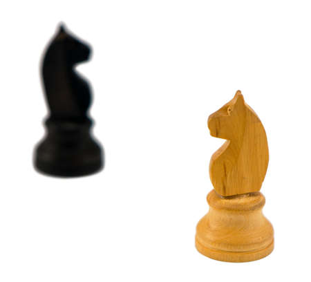 white wooden chess knight figure and blurred black one in distance on white backgroundの写真素材