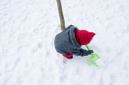 girl with a red hat in winter time with a green shovel dig snow の写真素材