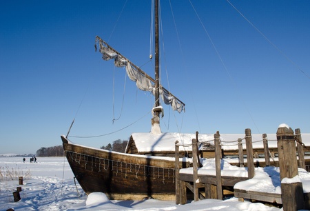 retro wooden ship frozen in lake ice near pier and sail on background of blue sky. people recreate in nature. の写真素材