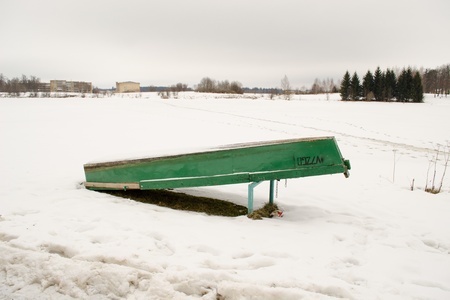 upturned wooden boat covered with snow rest on frozen lake shore bank waiting for warm season in winter. の写真素材
