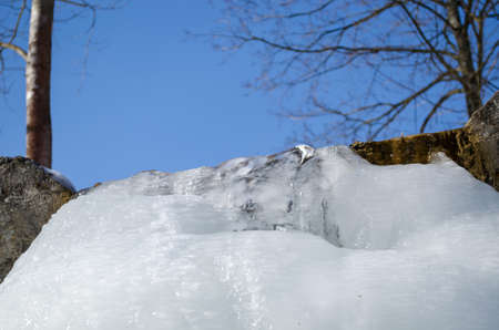 small park stream waterfall cascade covered with ice sulight and water flow under it on background...
