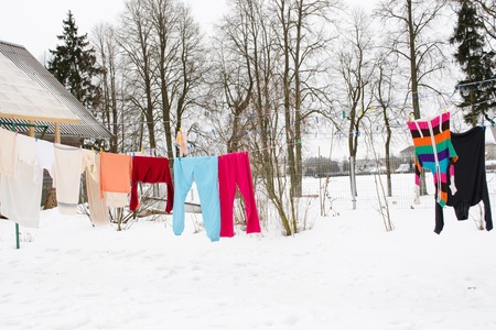 colorful washed wet clothes loundry dry hang on rope in house yard in winter. の写真素材