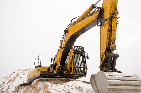 closeup of earthmover excavator stand on quarry pile sand pit soil earth covered with snow in...