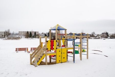 colorful playground on snowy frozen lake bank shore and living house district on other shore in...