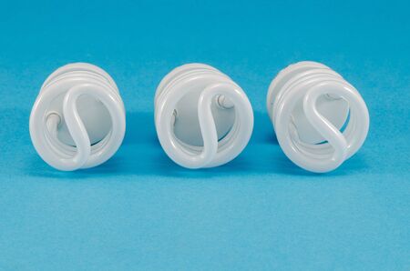 three new novel modern fluorescent light bulbs on blue background. modern technology use less...