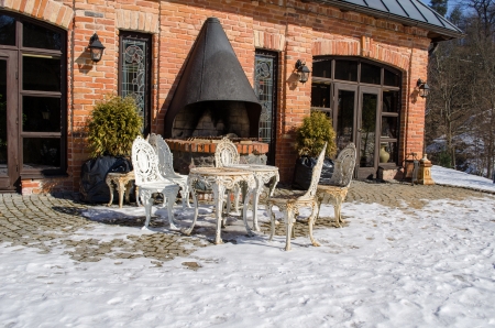 retro decorative outdoor table and chairs near restaurant fireplace building between snow in winter. の写真素材